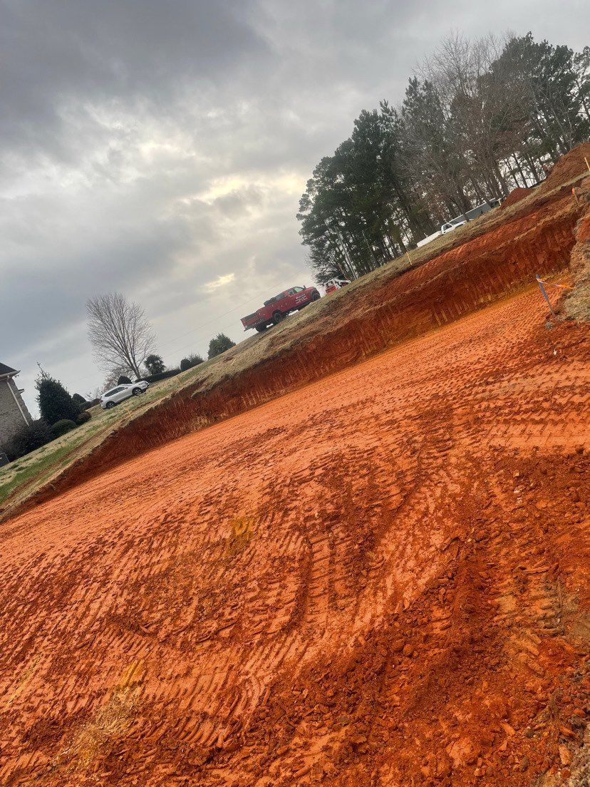 A dirt road with a red truck parked on the side of it.