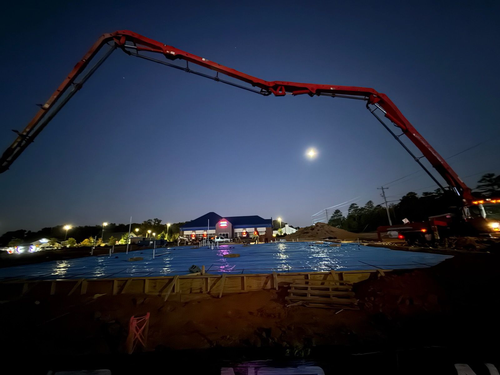 A concrete pump is being used to pour concrete into a pool at night.