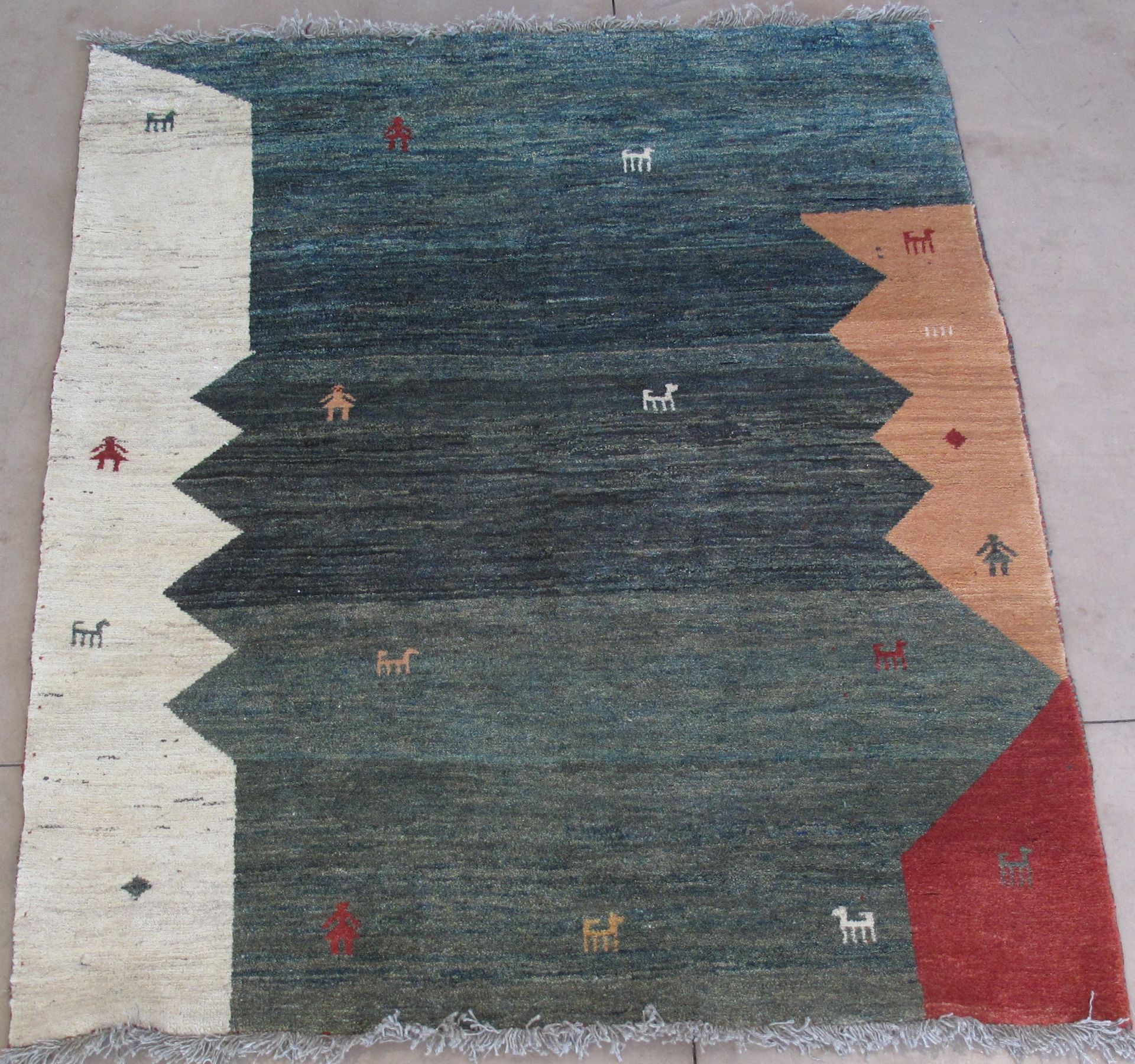 A rectangular rug featuring a dark blue, gradient center with geometric off-white, tan, and red borders and small motifs.