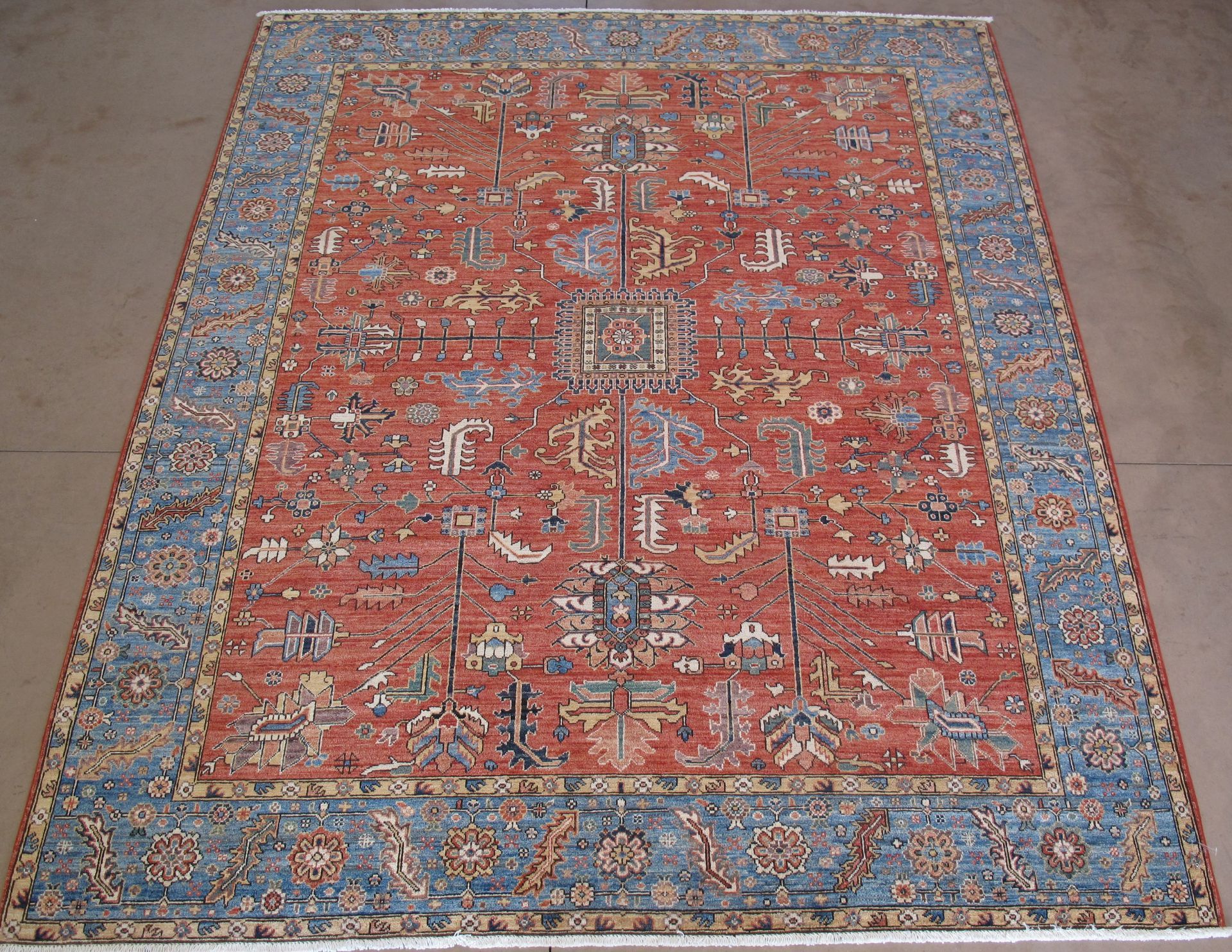 A large, rectangular rug featuring an intricate floral pattern in shades of red, blue, and cream on a light background.