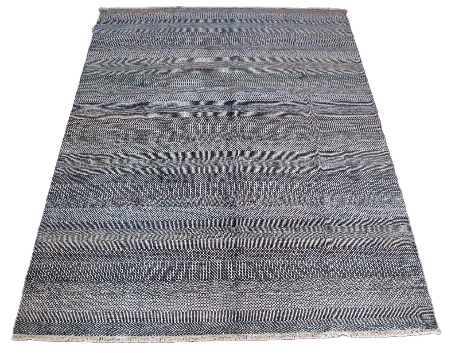 A close-up of a woven rug or fabric with a textured, repeating pattern in shades of dark blue, grey, and white.