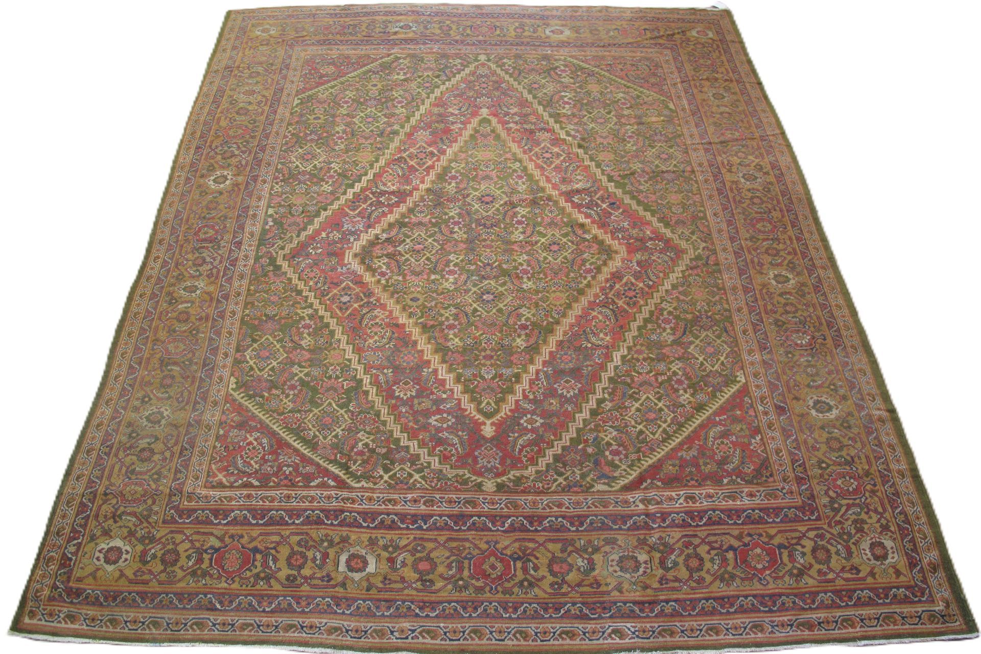 Large, ornate Persian rug with a central diamond design in red and beige, on a green field.