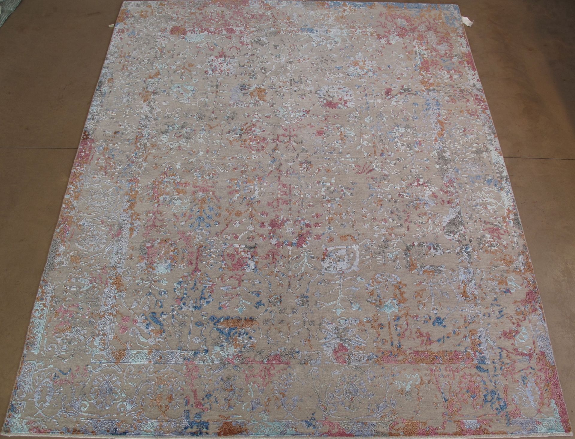 A rectangular area rug with a faded, distressed vintage pattern in shades of beige, muted orange, and soft blue.