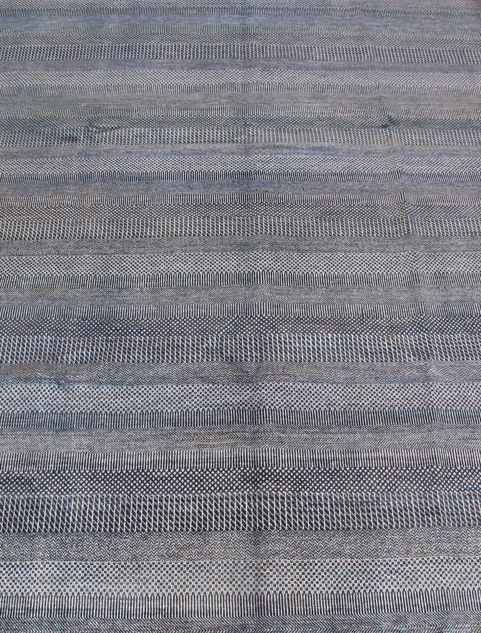 A close-up of a woven rug or fabric with a textured, repeating pattern in shades of dark blue, grey, and white.