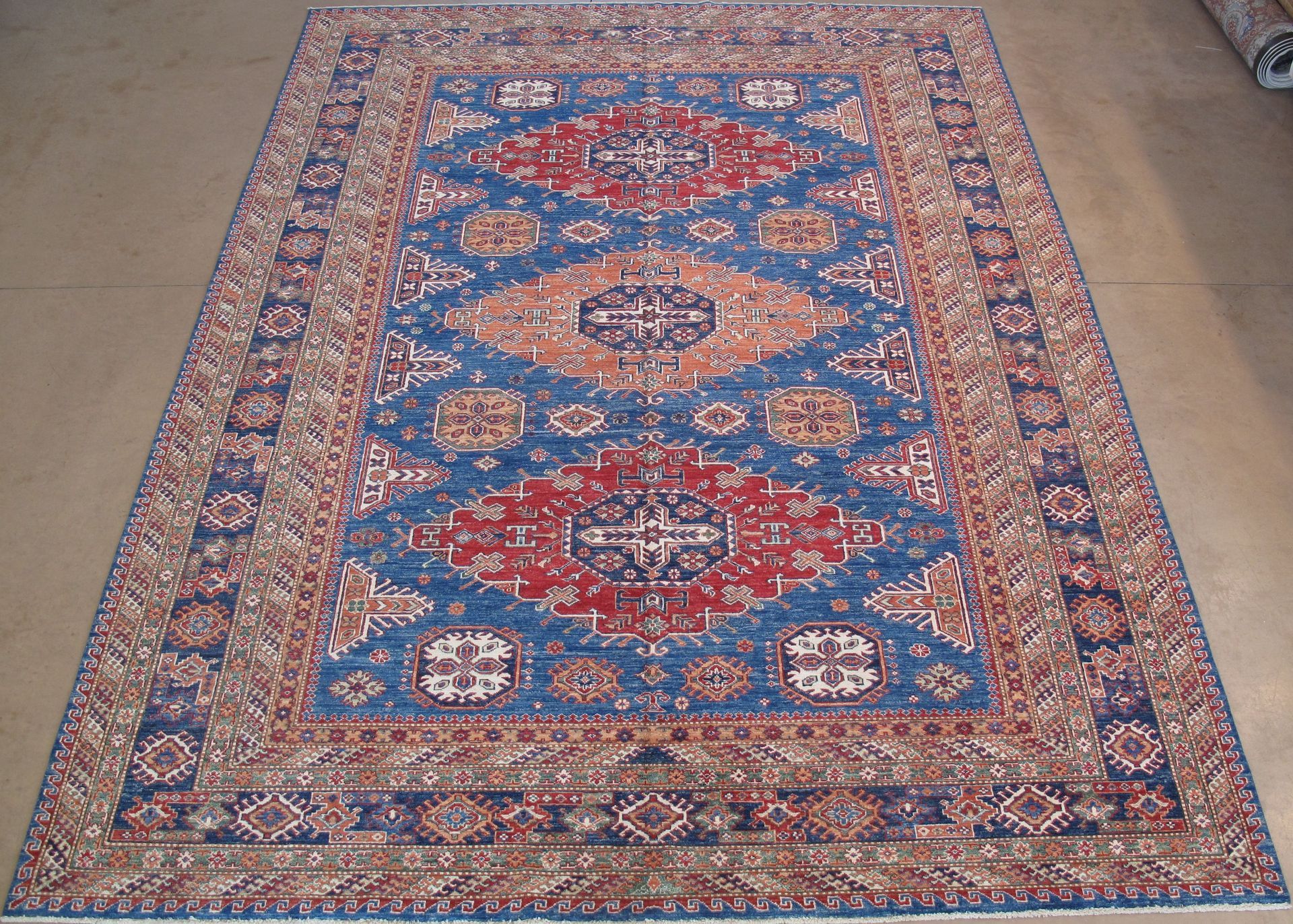 A rectangular rug with a blue field featuring red and tan geometric medallions and an ornate, patterned border.