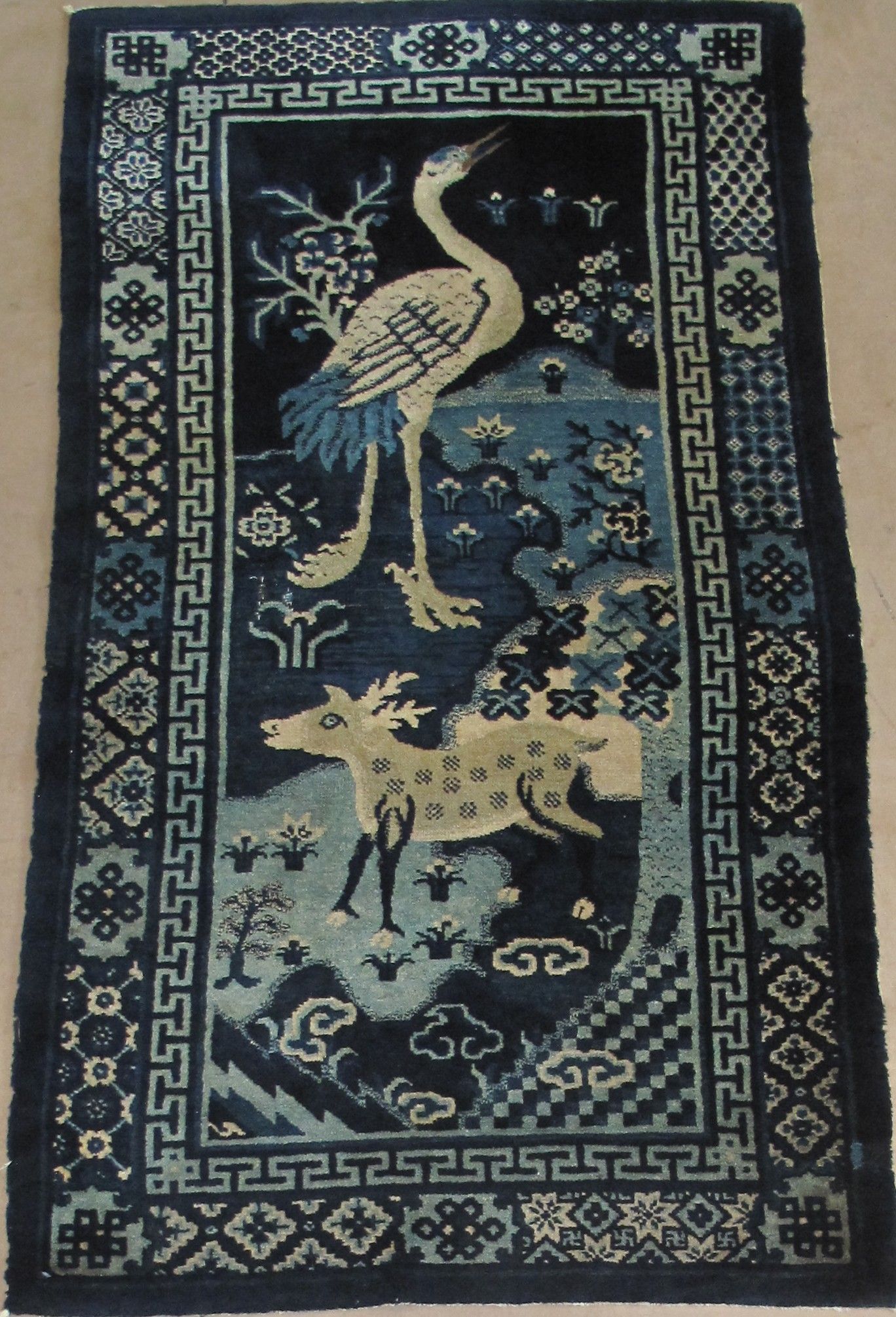 A rectangular dark blue rug featuring a crane, a spotted deer, and traditional geometric border patterns.