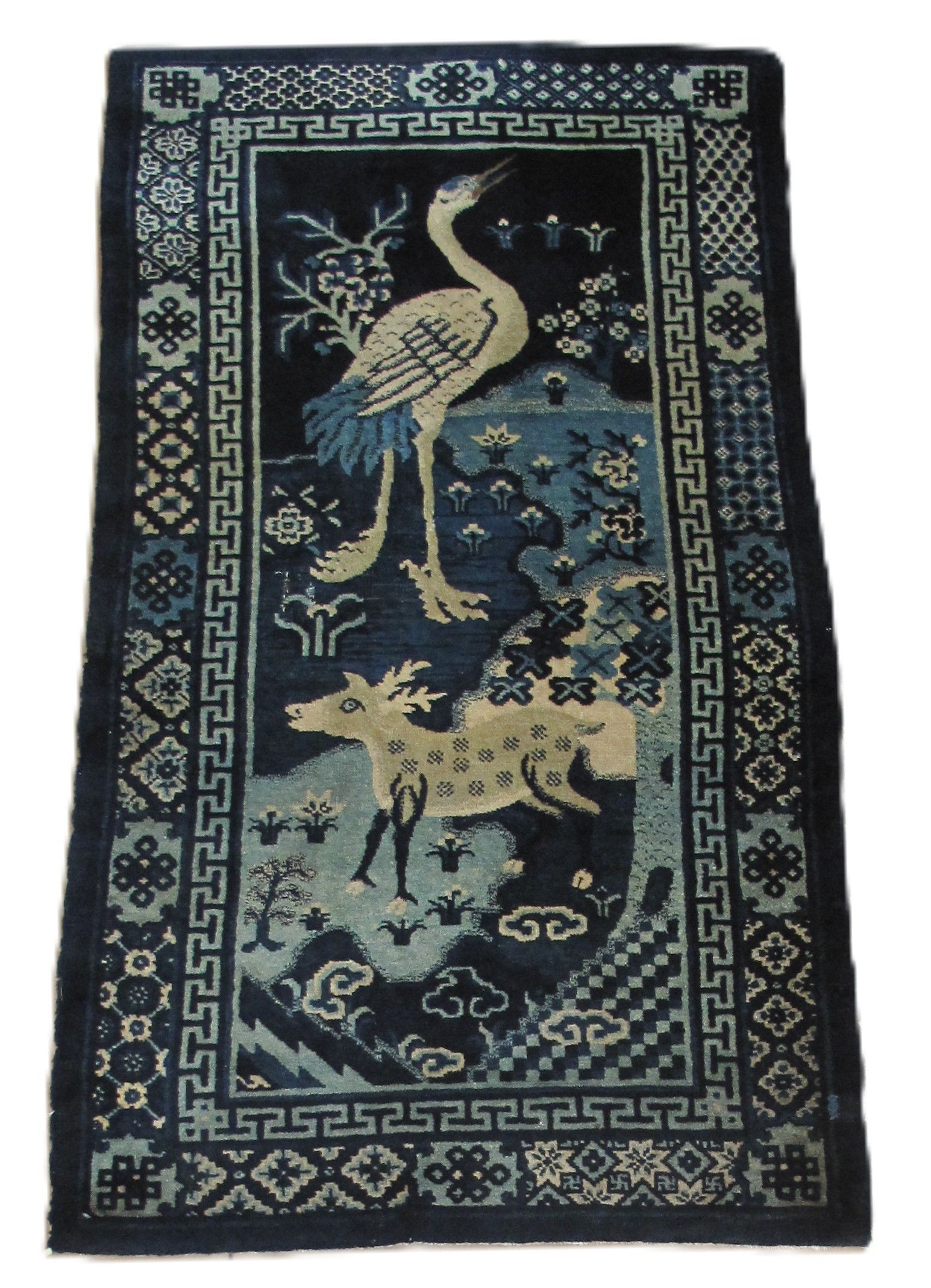 A rectangular dark blue rug featuring a crane, a spotted deer, and traditional geometric border patterns.