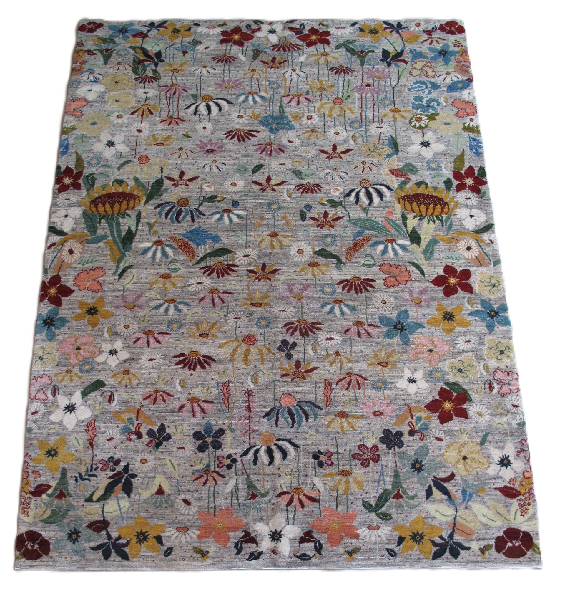 A rectangular area rug with a light gray background, densely patterned with a colorful variety of flowers and foliage.