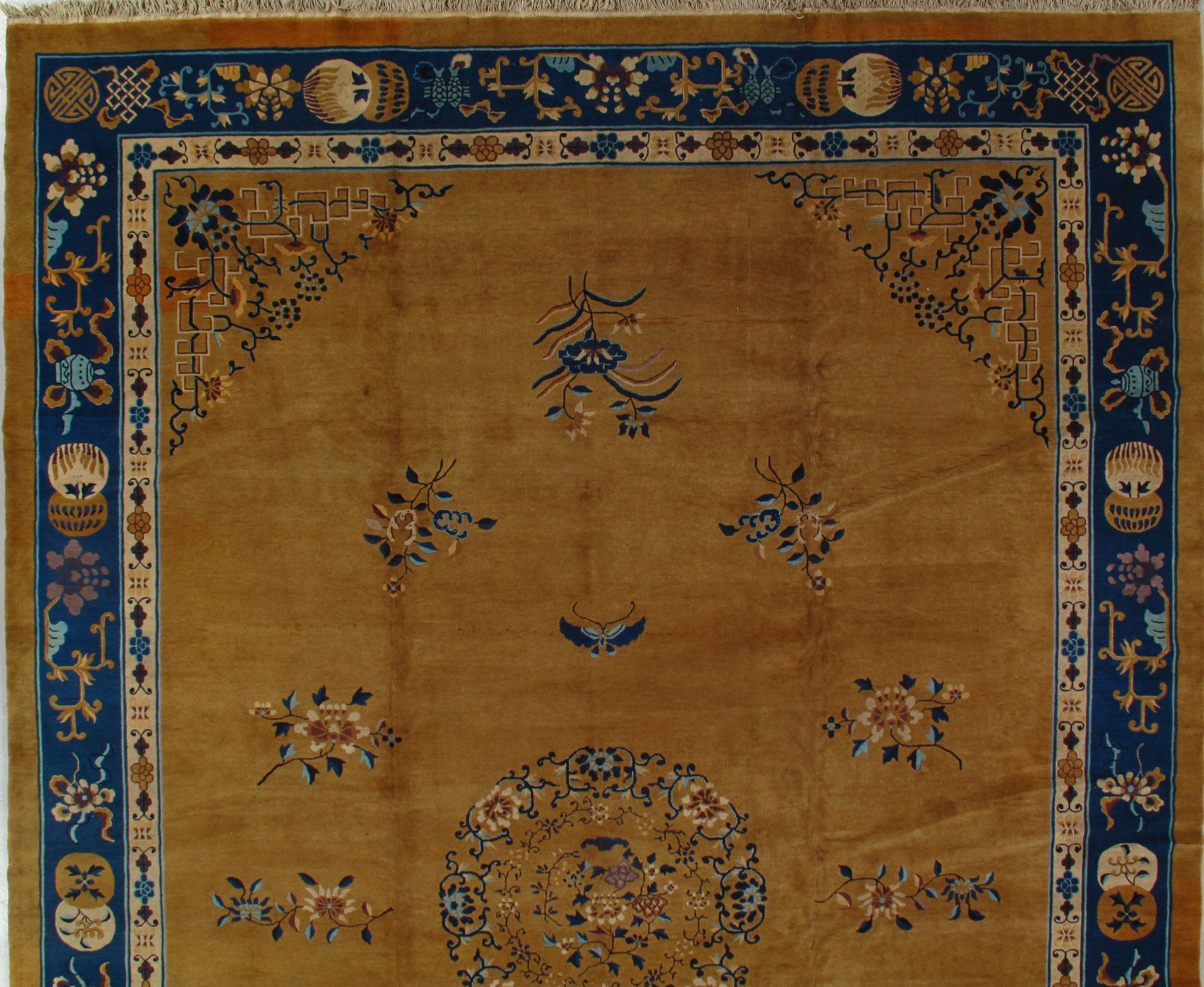 Close-up of a golden yellow oriental rug with blue floral border and center medallion design.