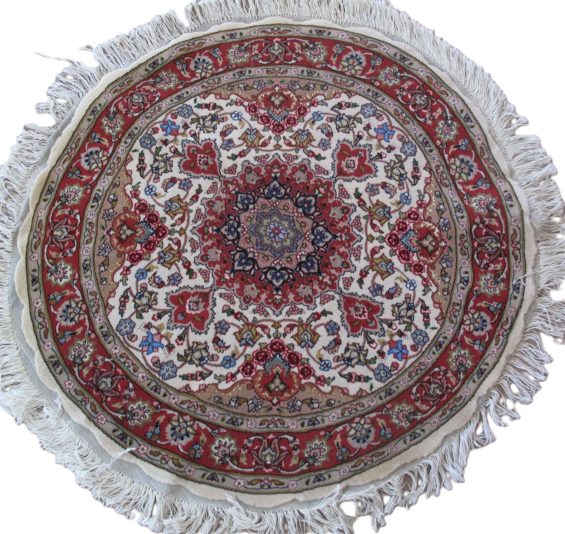 Round oriental rug with red, cream, and blue floral design and fringe.