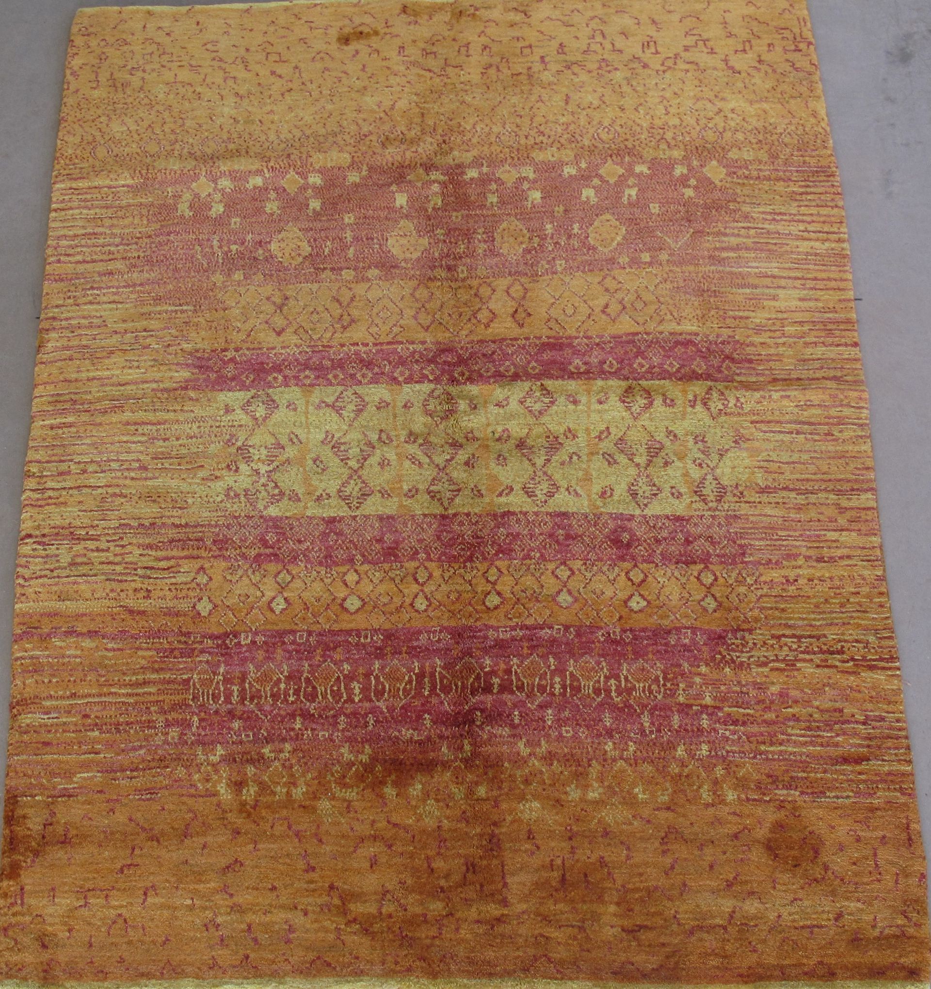 A rectangular carpet with a golden background. It features red horizontal bands with geometric patterns.