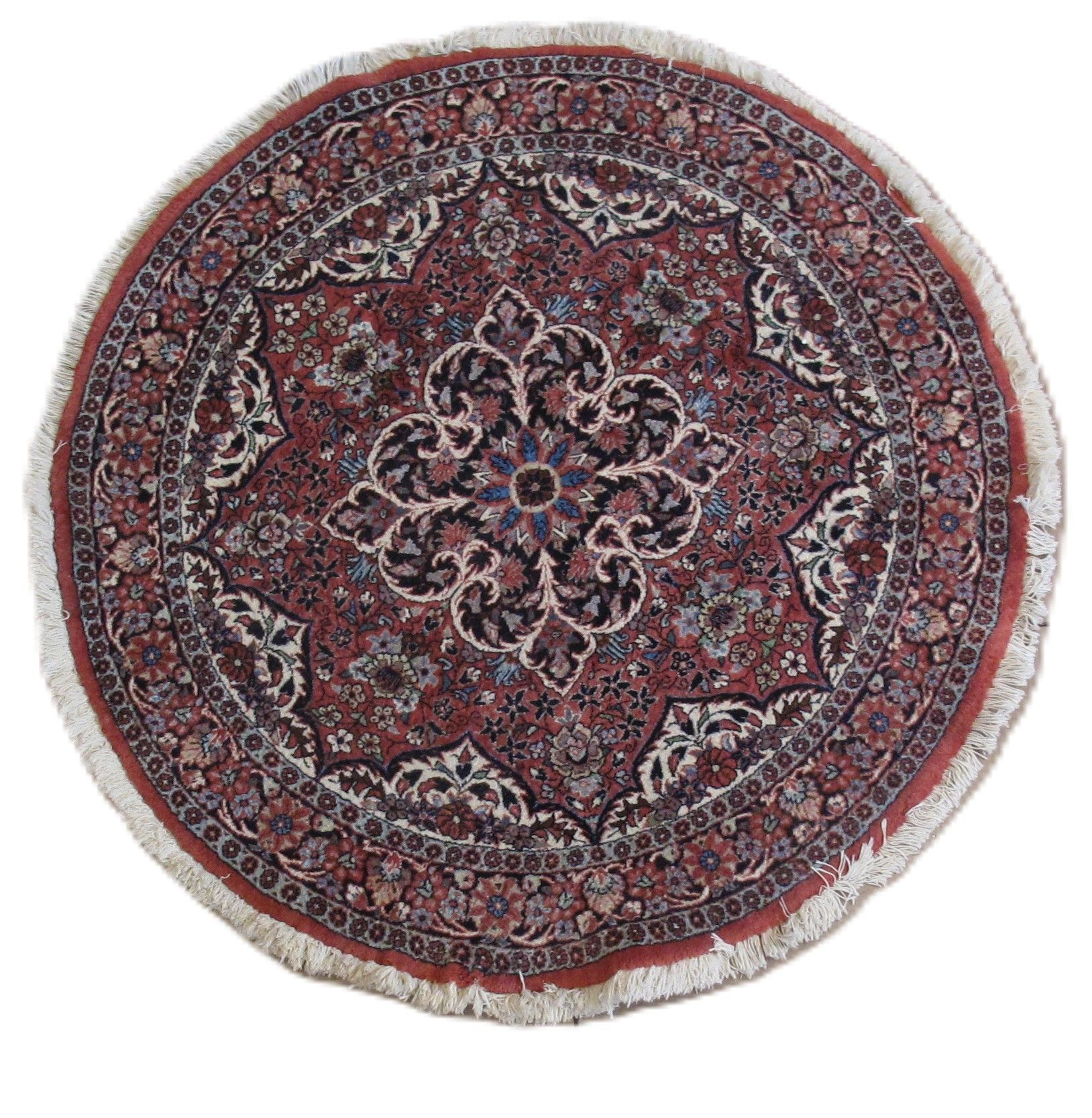 A round Persian-style rug with an intricate floral medallion pattern in red, blue, cream, and black, featuring white fringe.