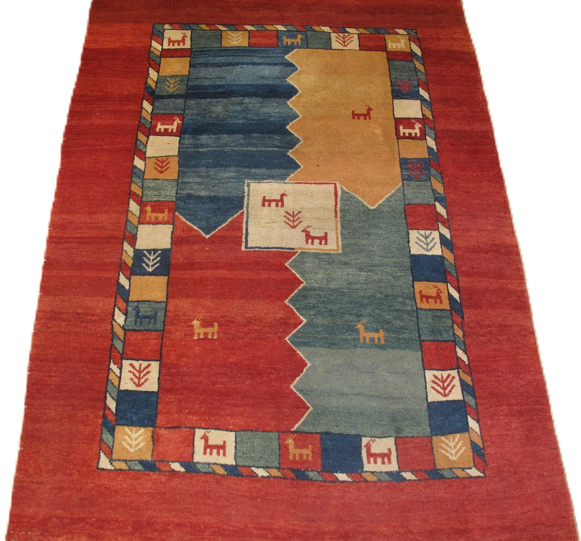 Red rug with blue, tan, and red geometric shapes. Bordered with colorful squares and animal motifs.