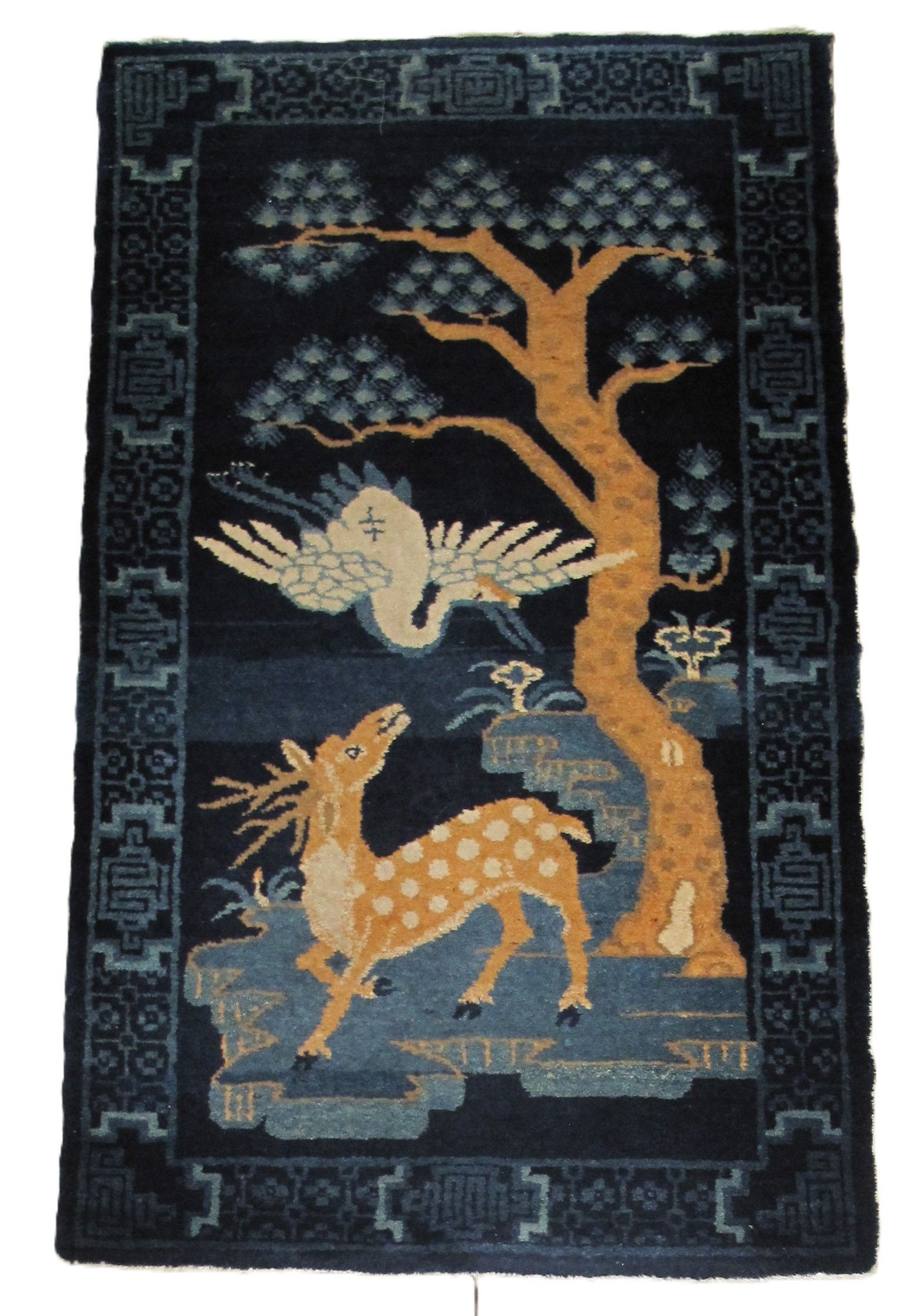 Dark rug with deer, crane, and tree designs, blue, tan, and white.