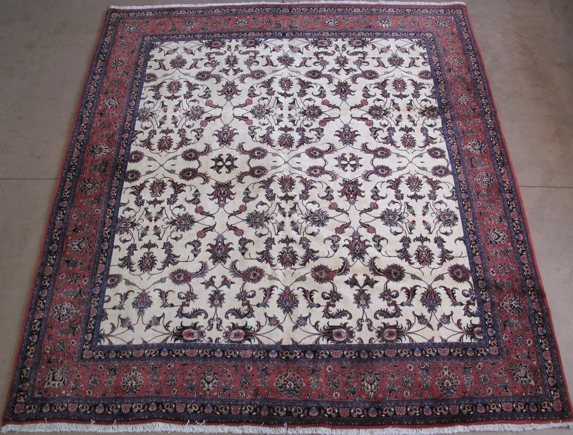 An ornate, rectangular area rug featuring a cream-colored field with floral patterns, bordered by deep red and navy tones.