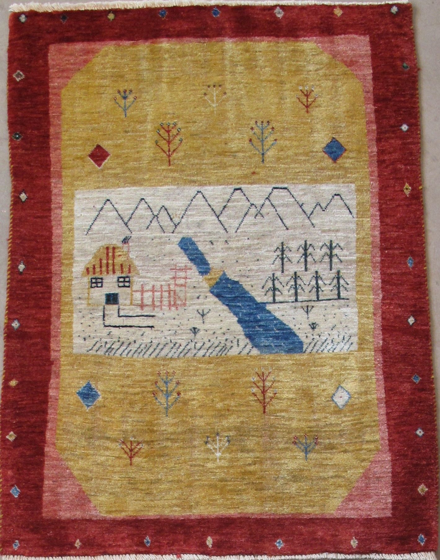Rug with a yellow-toned center, red border, and a scene of a house, mountains, and a river.