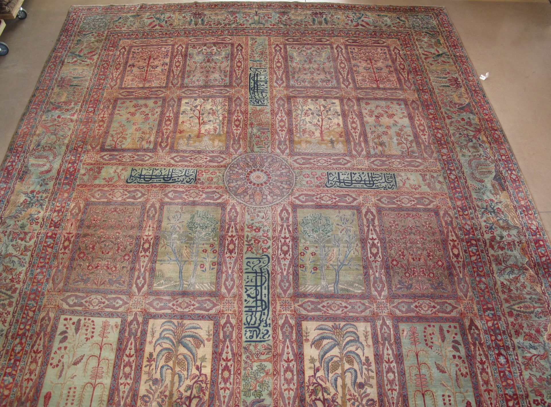 A large, rectangular rug featuring a grid of ornate, pale floral panels set against a pink-toned, patterned field.