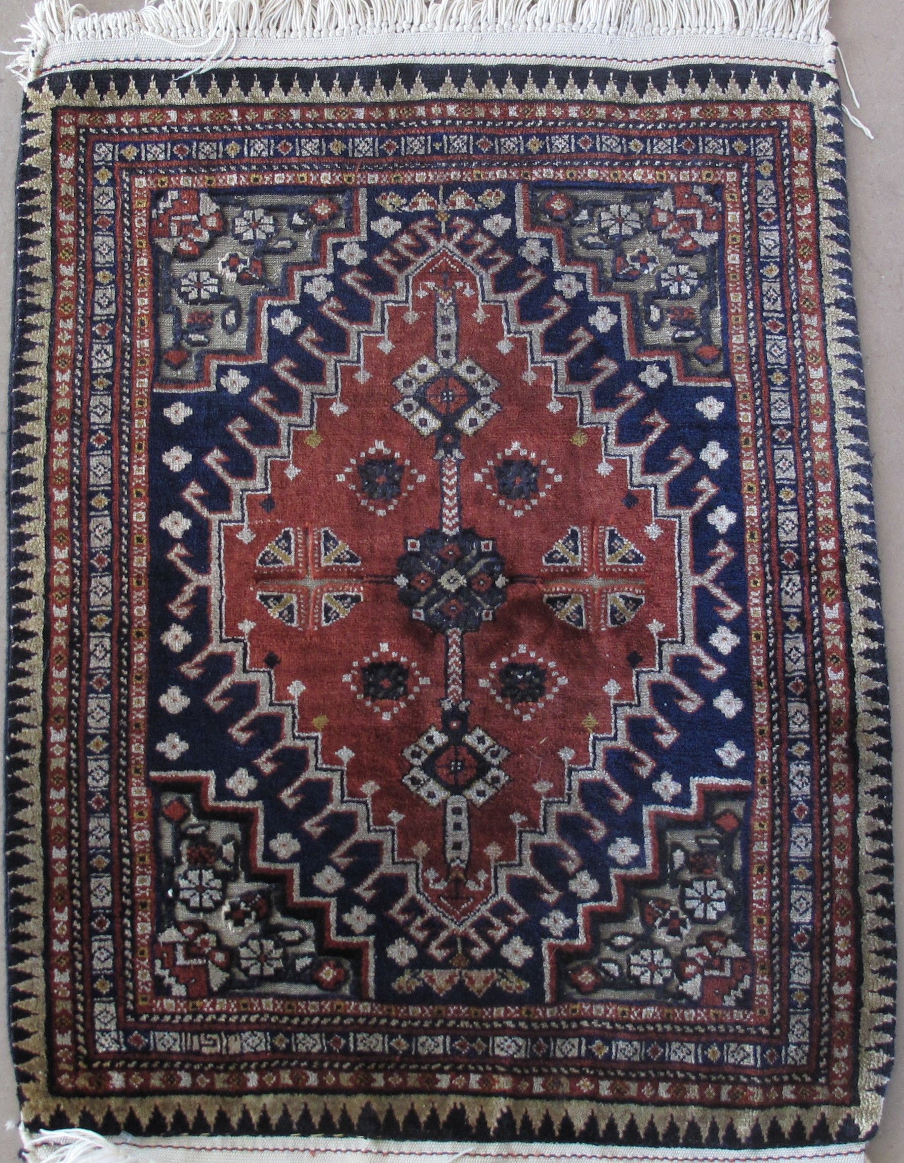 Small, square rug with a central diamond pattern in red, surrounded by blue and patterned borders.