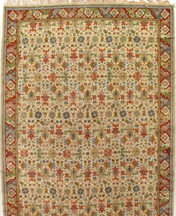 Cream-colored rug with ornate floral and geometric patterns in red, green, blue, and gold, with a red border.