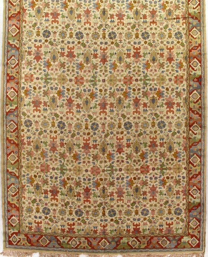 Cream-colored rug with ornate floral and geometric patterns in red, green, blue, and gold, with a red border.