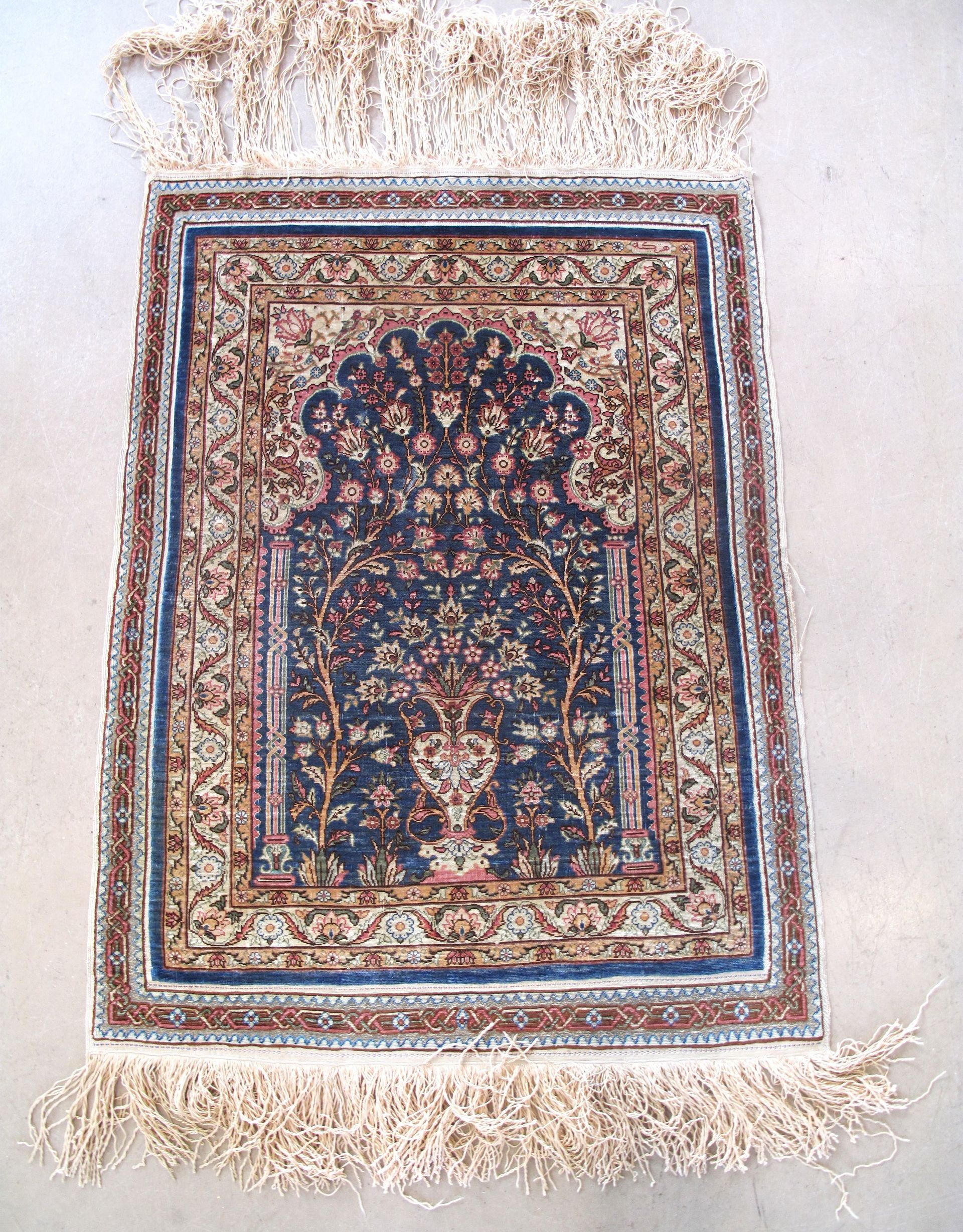 A rug with a floral pattern and fringe is hanging on a wall