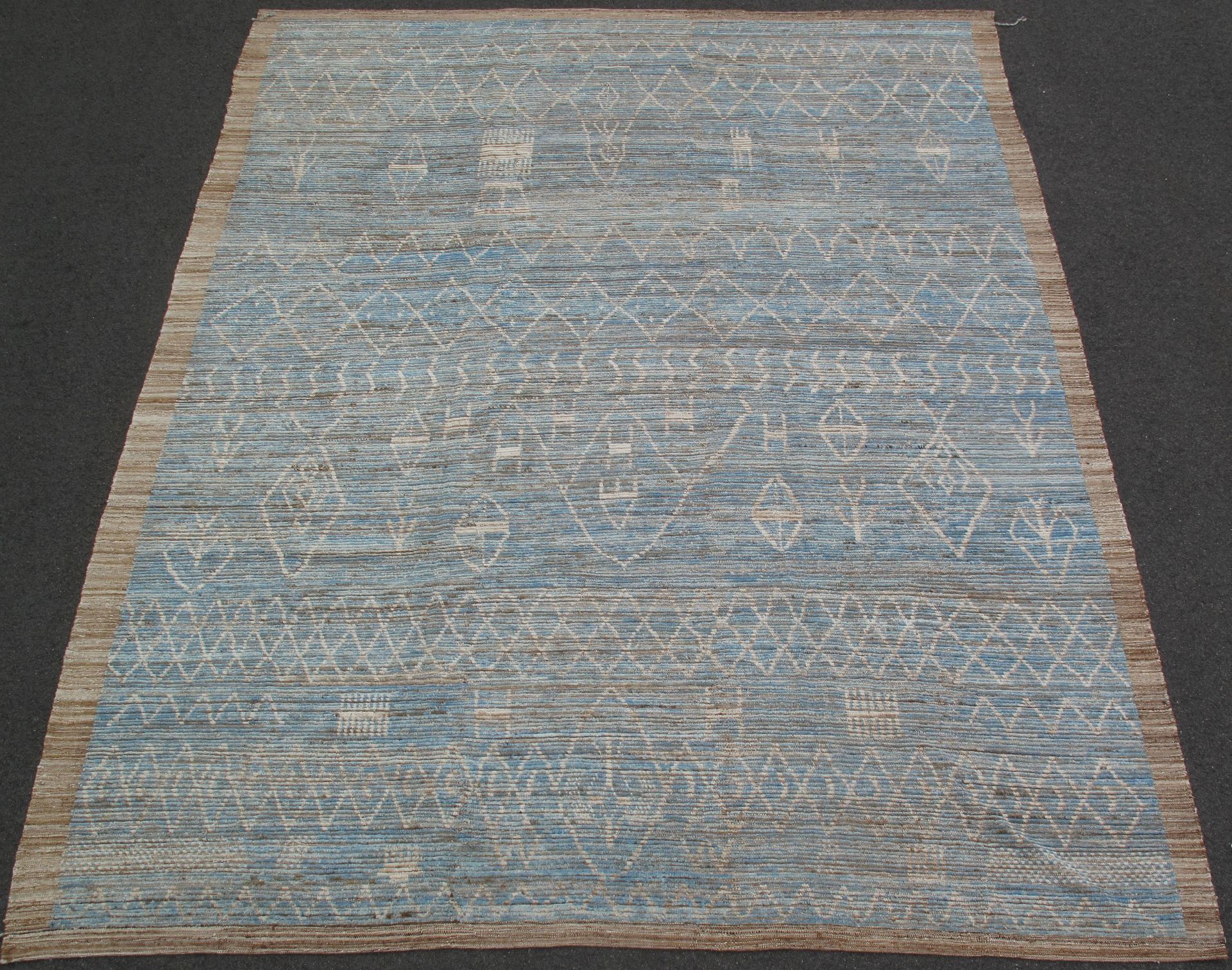 Blue-gray textured area rug with tan edges on a white background