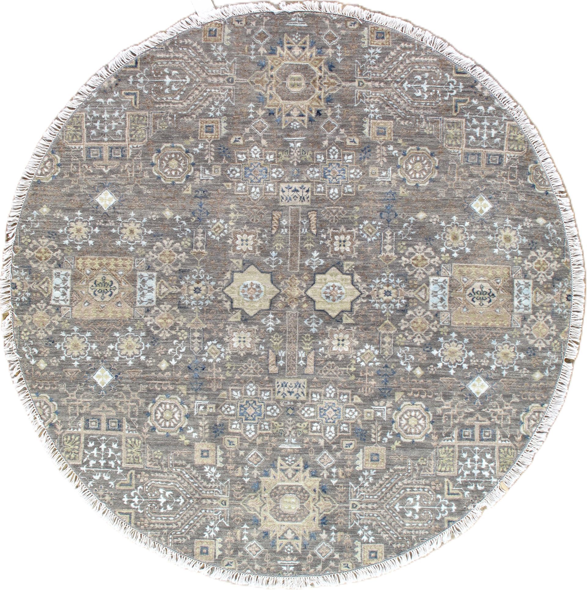 Round, gray, patterned rug with fringe. Features symmetrical, detailed design in muted tones.