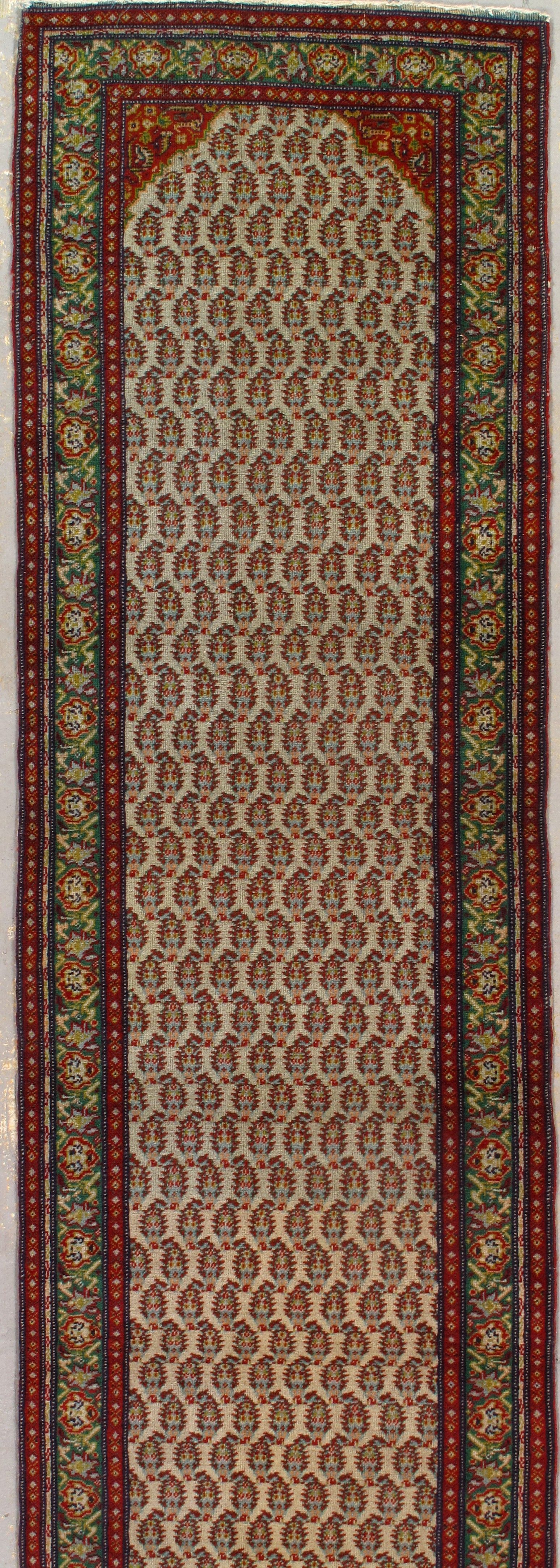 Long, narrow rug with a patterned center, bordered by red and green floral designs.