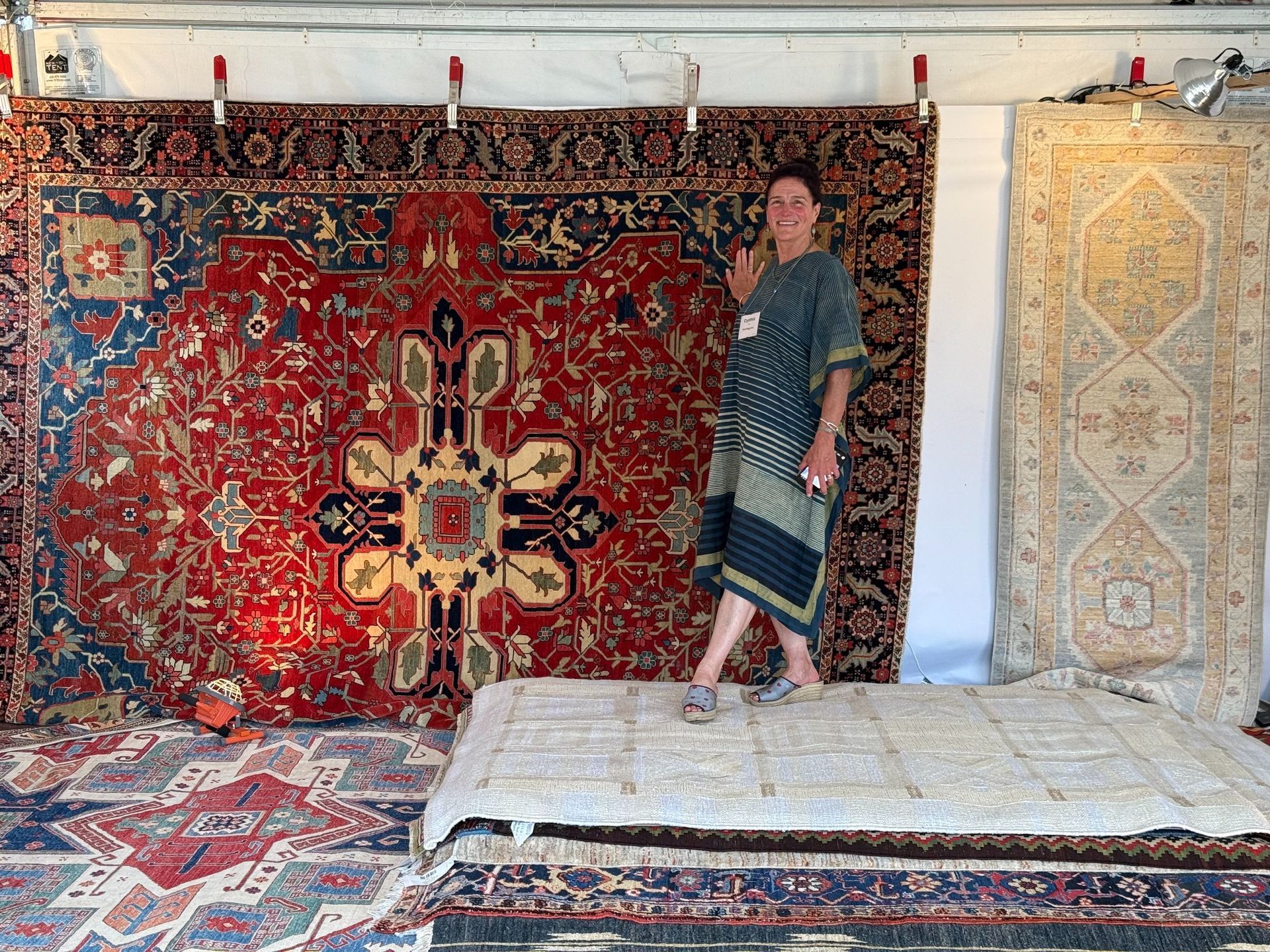 Cynthia standing beside large red and cream patterned rugs hanging in a showroom