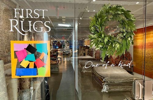 Storefront window display for First Rugs with a colorful rug sample and a large green wreath behind glass