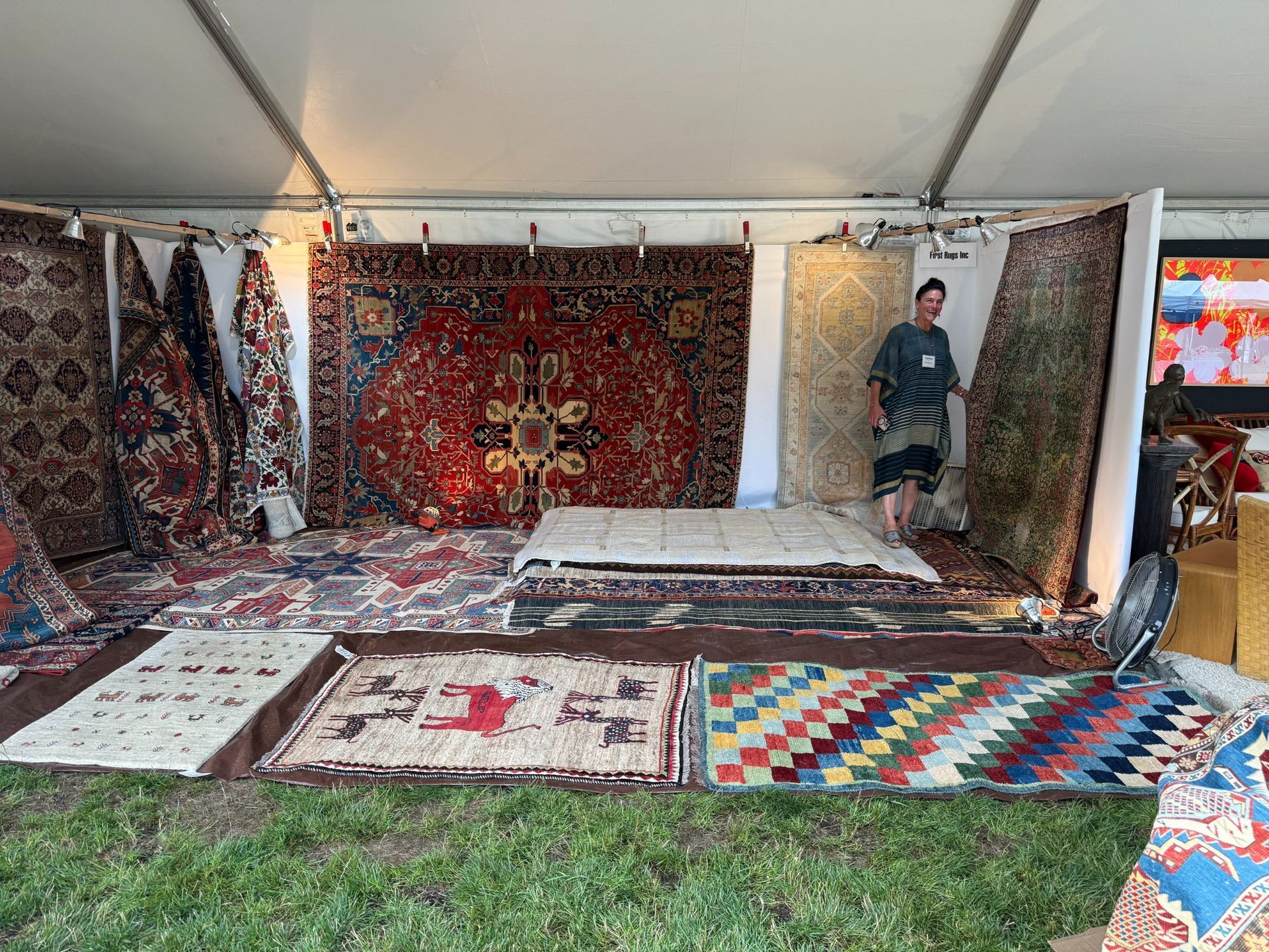 Cynthia First is standing in a festival booth surrounded by antique rugs. 