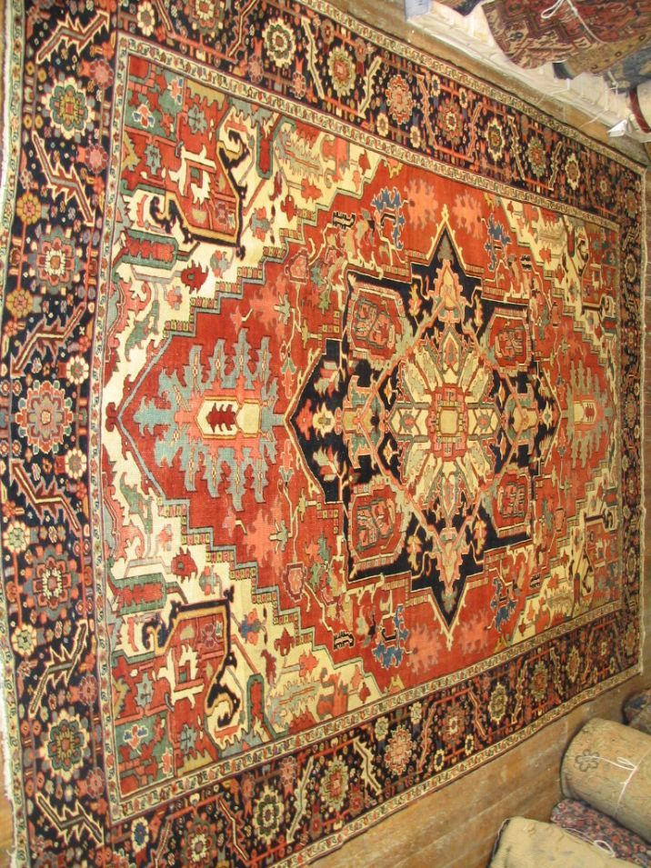 Colorful red and gold patterned serapi rug with geometric medallion hanging on a wall