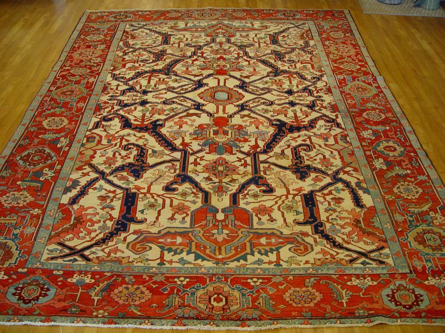Red and cream patterned serapi rug on a wooden floor, seen from above.
