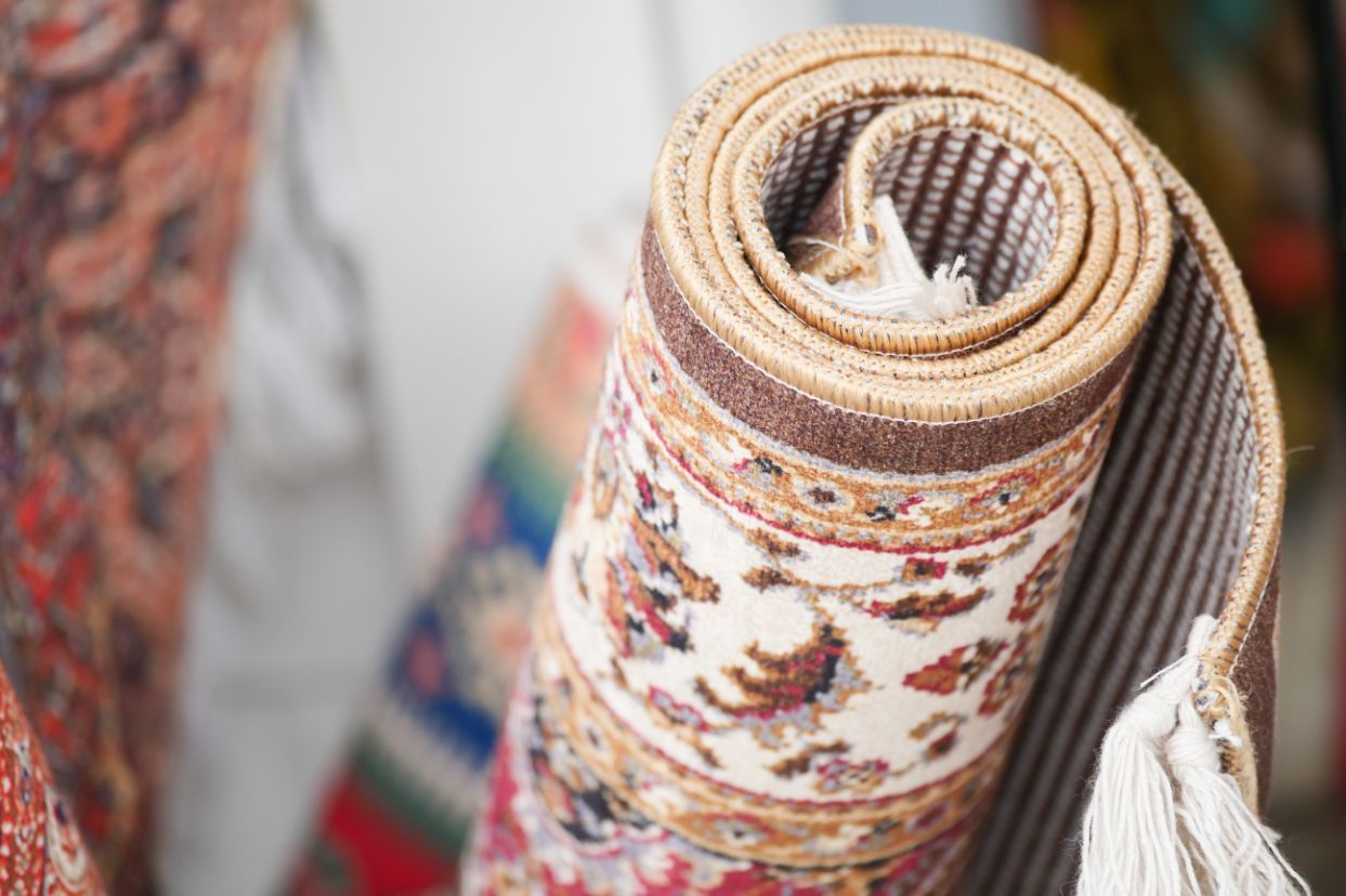 Rolled-up patterned carpet with beige and brown border, tassels visible.
