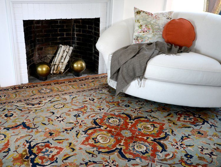 White chair by a black fireplace with pillows and a colorful patterned rug in a cozy living room