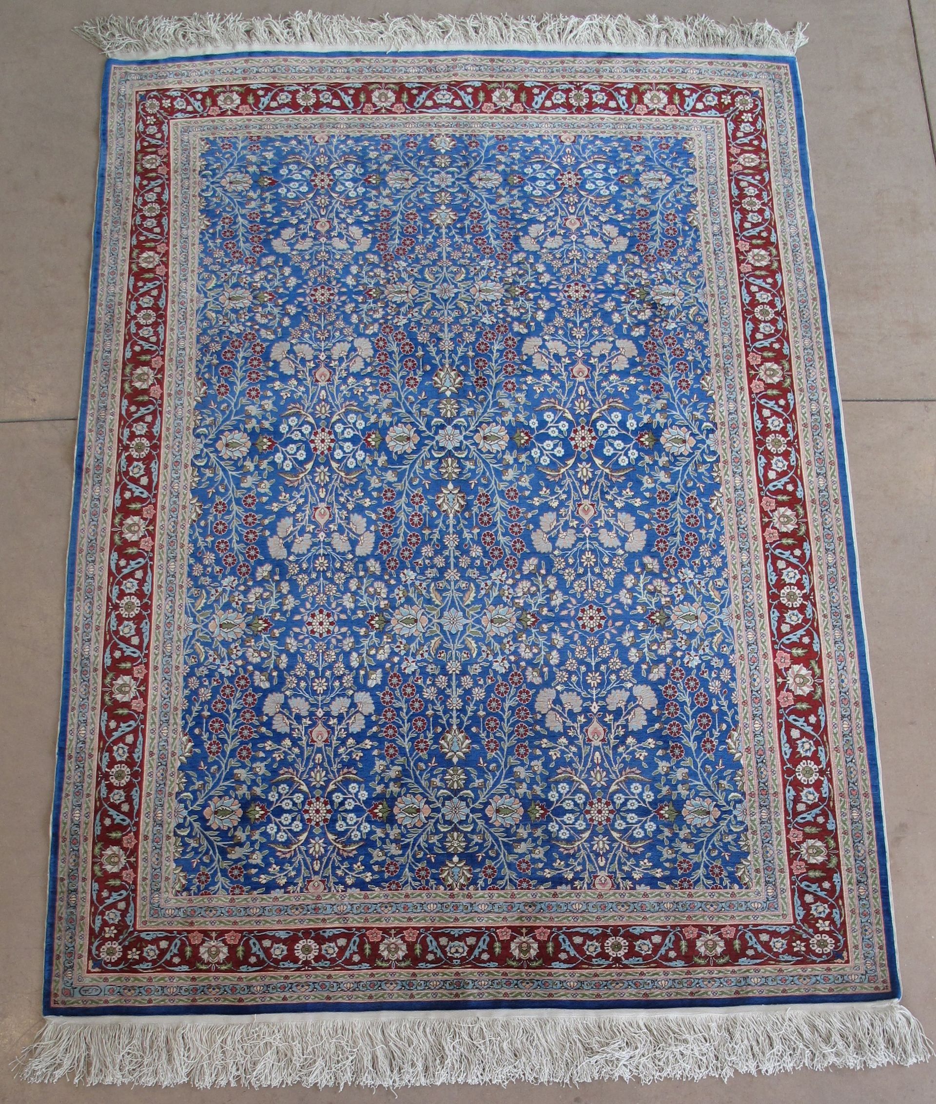 Blue rectangular rug with red and white border and fringe.
