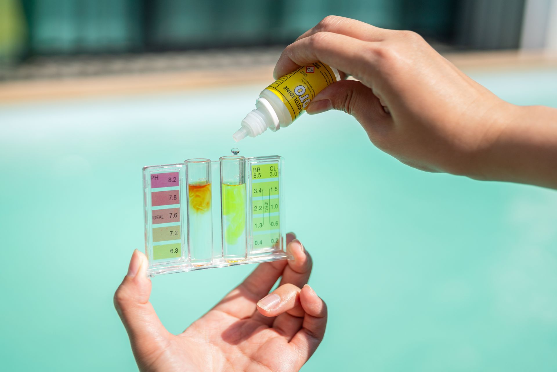 Hands dropping liquid into pool water test tubes.