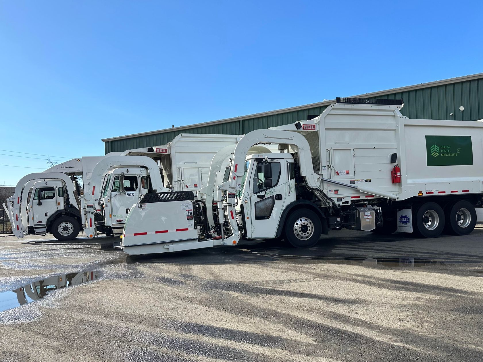 Three garbage trucks are parked next to each other in a parking lot.