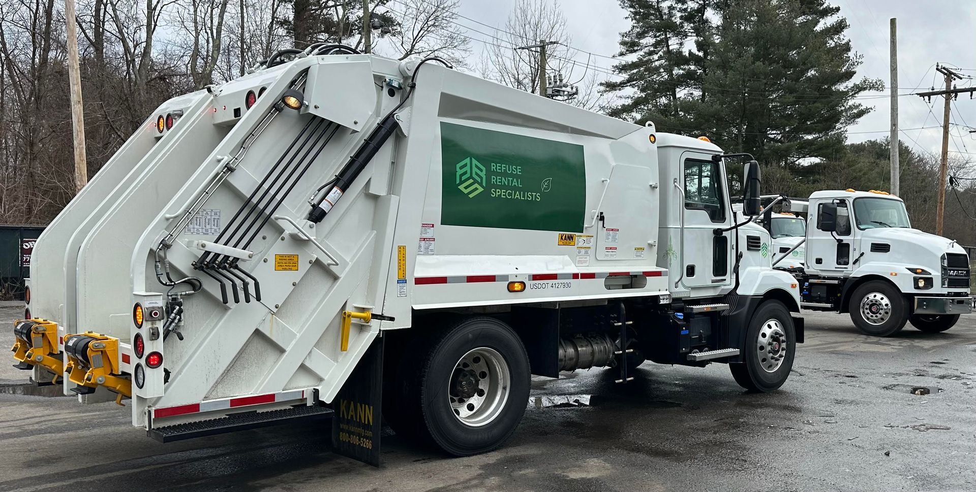 A garbage truck is parked next to another garbage truck in a parking lot.
