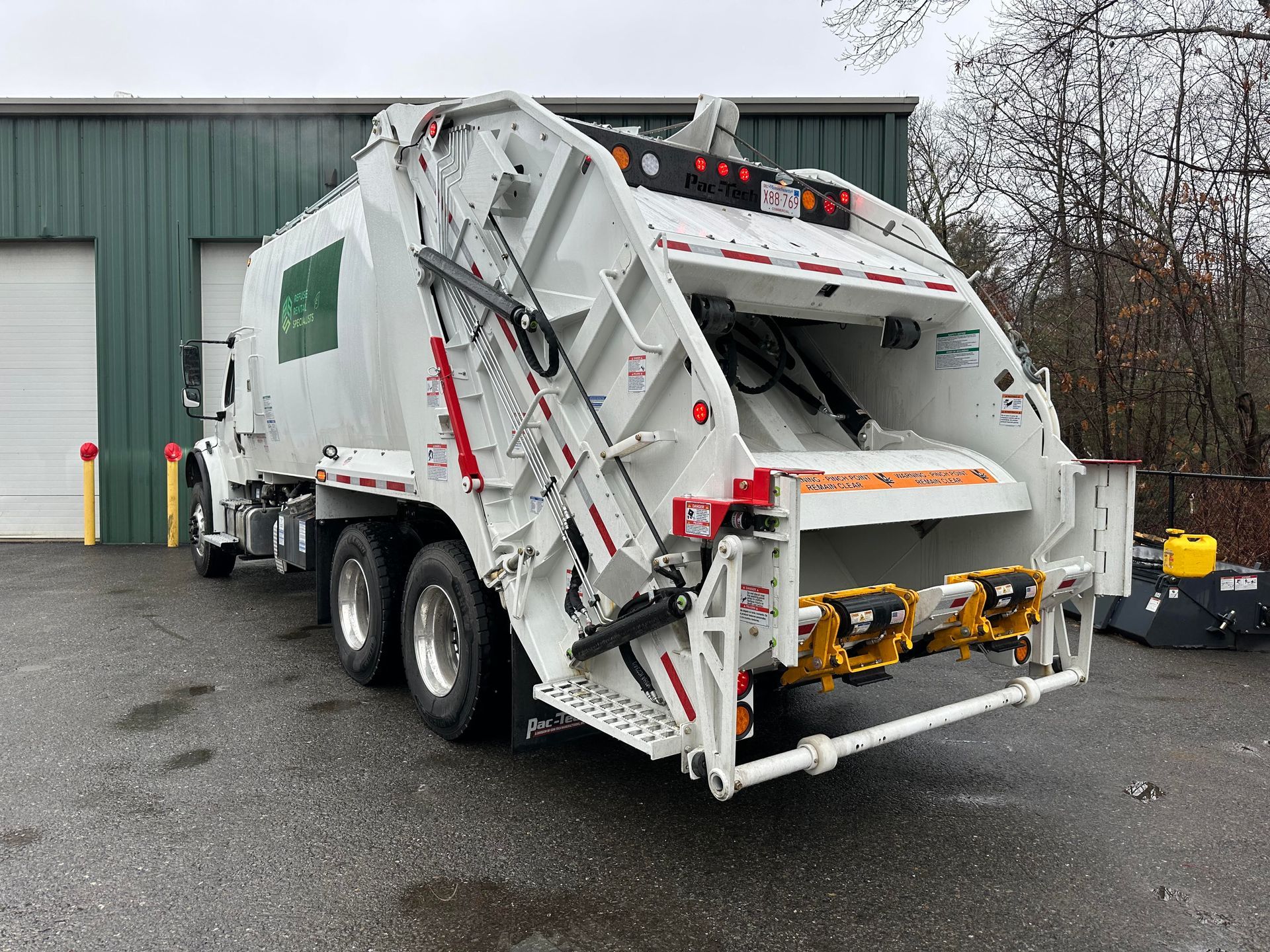A white garbage truck is parked in front of a green building.
