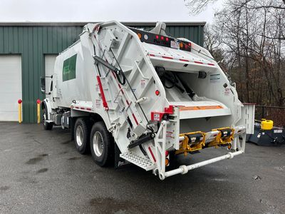 A white garbage truck is parked in front of a green building.