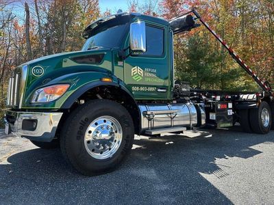 A green dump truck is parked on the side of the road.