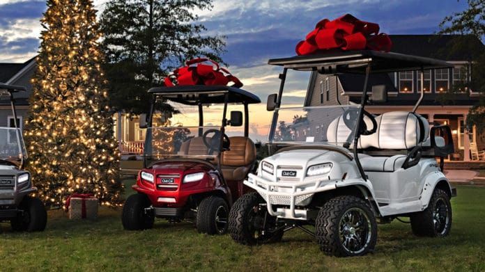 Three golf carts are parked in front of a house with a christmas tree in the background.