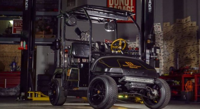A golf cart is sitting on a lift in a garage.