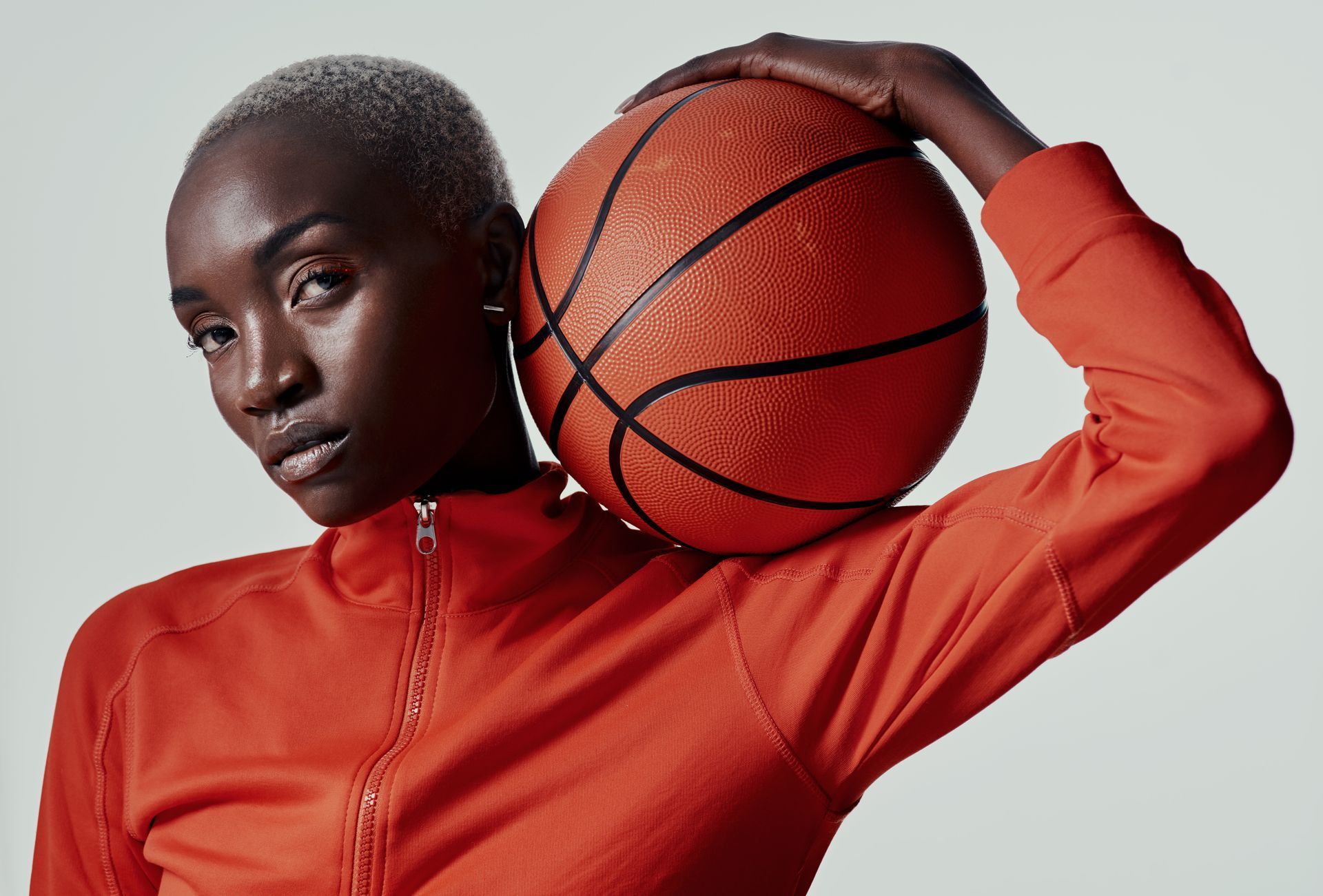 Person holding a basketball, wearing an orange top against a plain beige background.