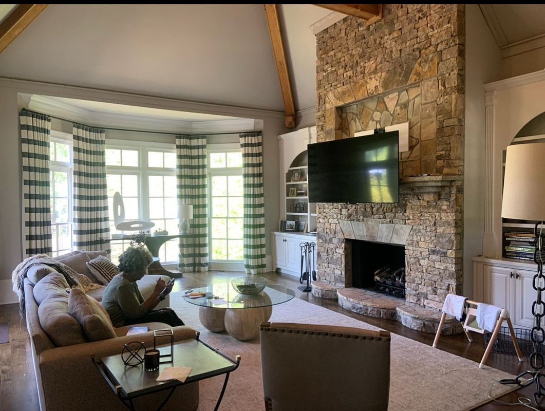 Cozy living room with stone fireplace, wall-mounted TV, sofa, and bright windows with striped curtains