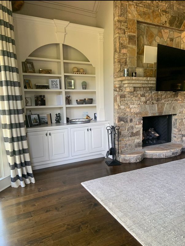 Living room with built-in white shelves, stone fireplace, wall TV, and hardwood floors