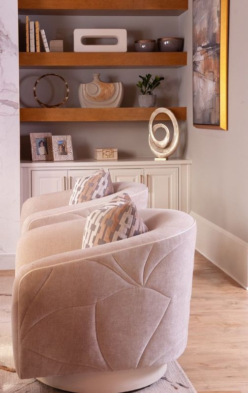 Plush beige armchair in a warm, modern living room with wooden shelves and decorative accents