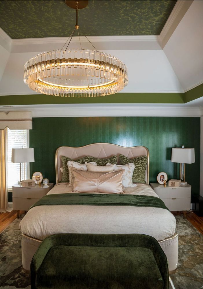 Elegant bedroom with a tufted bed, green accent wall, and gold chandelier.