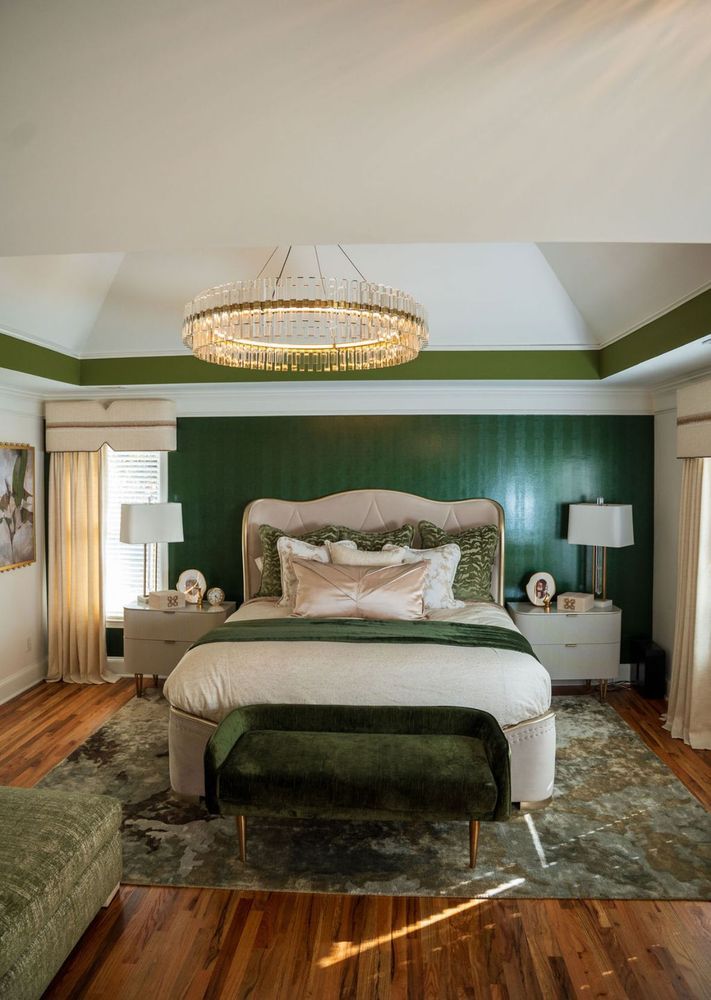 Elegant bedroom with a bed, green accent wall, chandelier, and patterned rug.